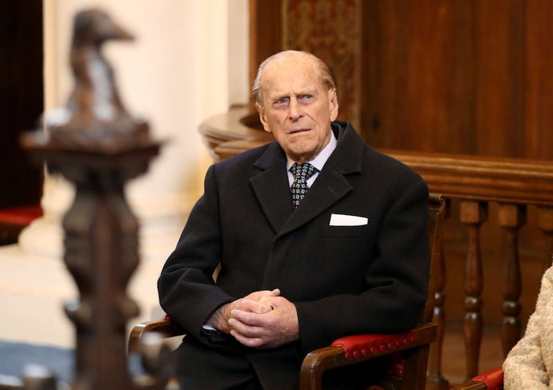 Prince Phillip sitting in a chair while wearing a black jacket and tie. 