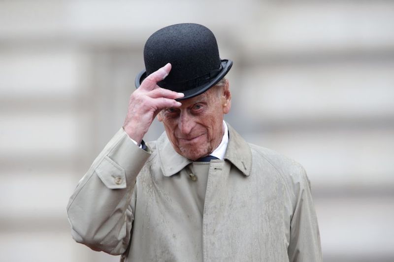 Prince Phillip holds his hat while standing in the rain. 
