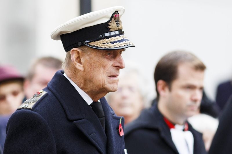 Prince Phillip walking straight forward while dressed in a naval uniform.