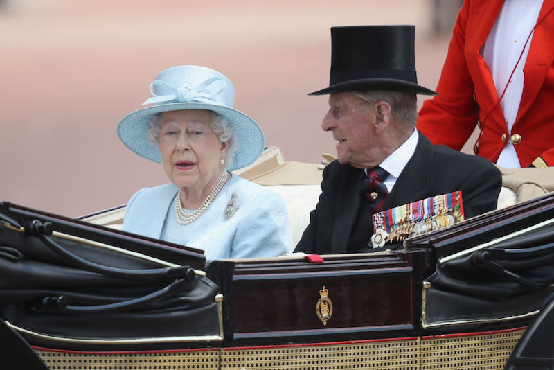 Queen Elizabeth and Prince Phillip riding in a coach. 
