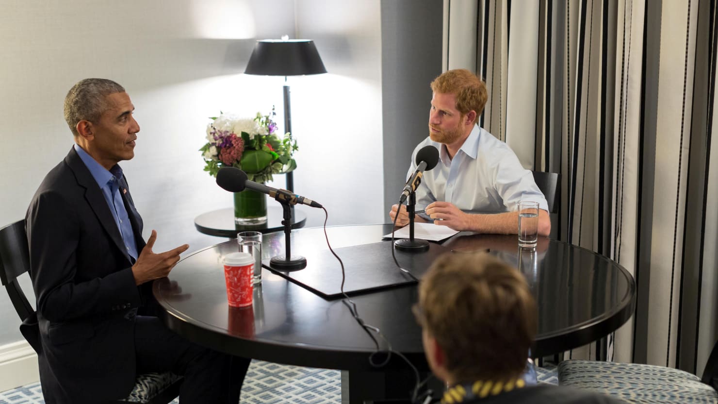 Prince Harry and Barack Obama sit at a round table in front of microphones Prince Harry and Barack Obama sit at a round table in front of microphones