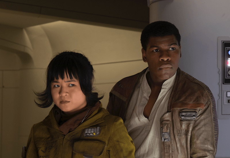 Rose and Finn stand close together and focus on something in front of them. 