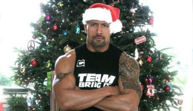 Dwayne Johnson stands in front of a Christmas tree in a Santa hat with his arms folded Dwayne Johnson stands in front of a Christmas tree in a Santa hat with his arms folded