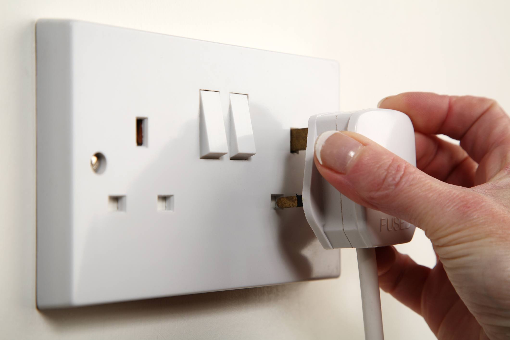 Hand plugging a plug into a grounded, British socket