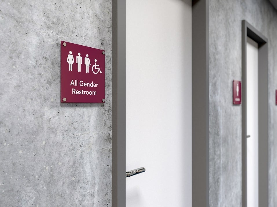 An all gender rest room sign next to a bathroom door