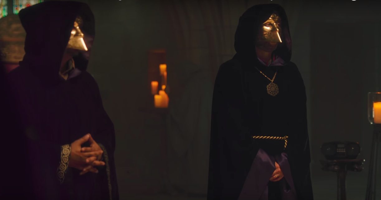 Two men dressed in cloaks and face masks.