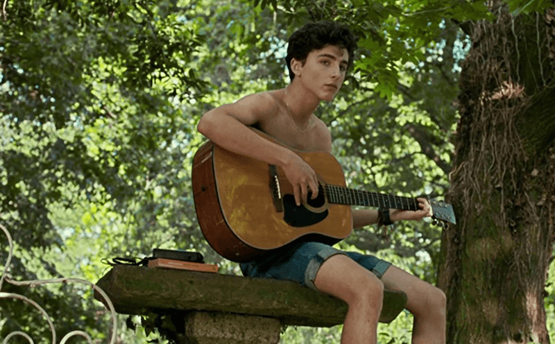A young boy plays a guitar while sitting at a bench. A young boy plays a guitar while sitting at a bench.