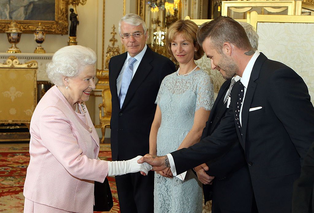 Britain's Queen Elizabeth II (L) shakes hands with former England footballer David Beckham (R) as former prime minister John Major (2L) looks on during a reception