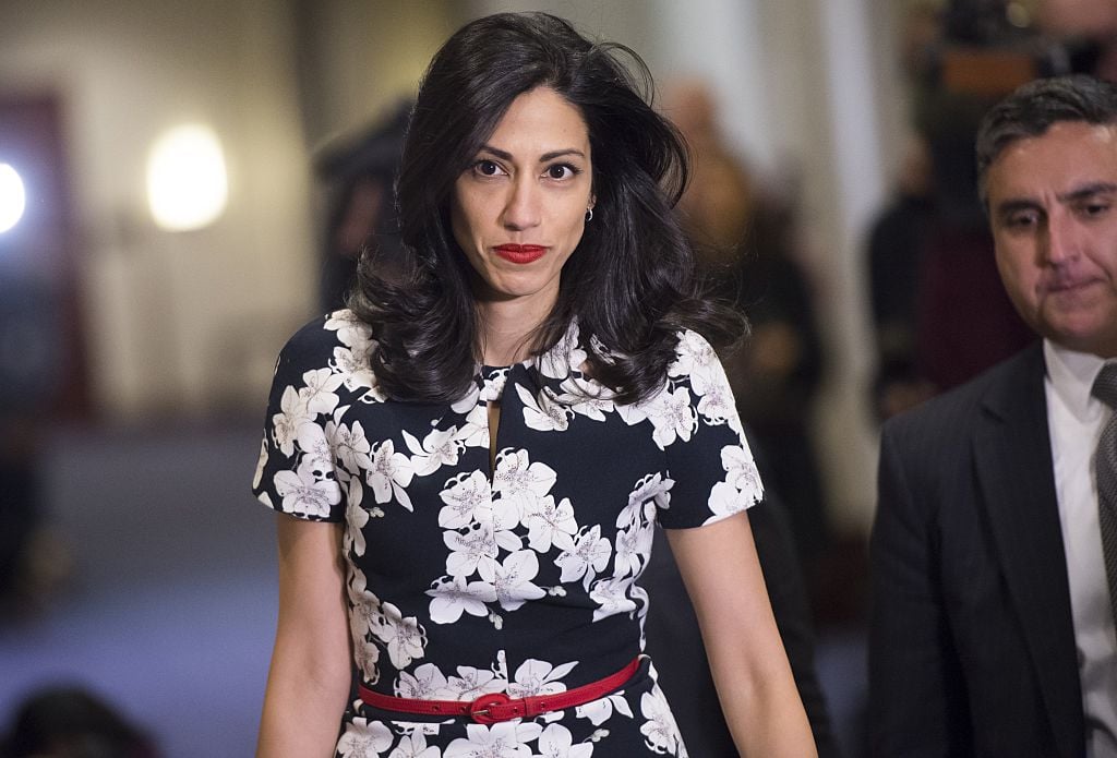 huma abedin walking in a black and white floral dress and red belt