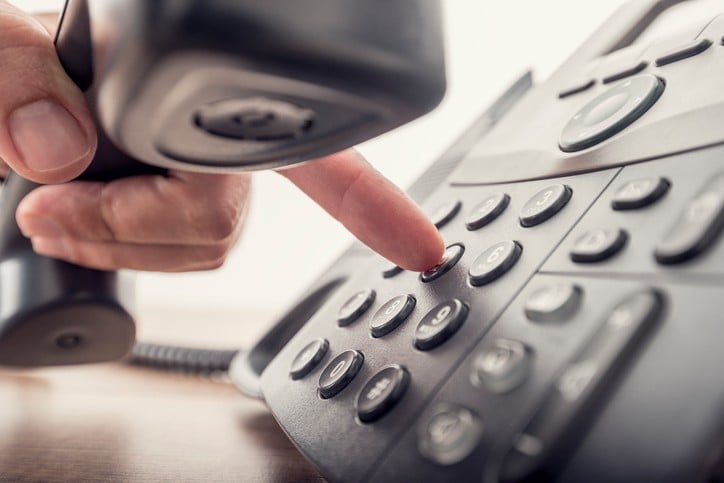 Closeup of hand holding telephone receiver while dialing
