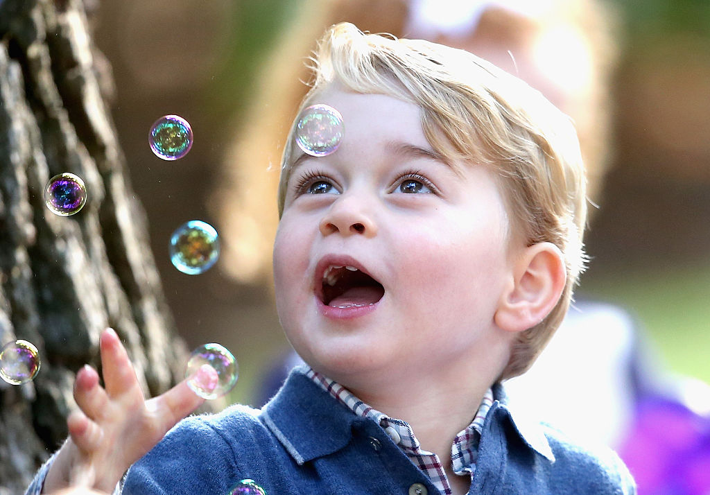 Prince George looks happily at bubbles in the air.