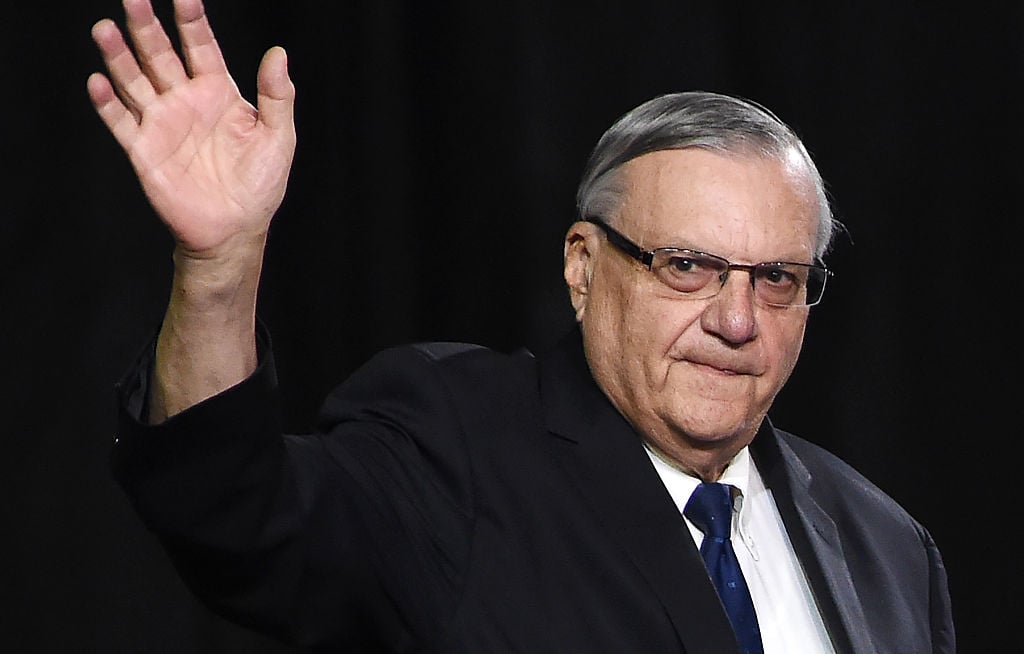Joe Arpaio in a black suit waving at a crowd