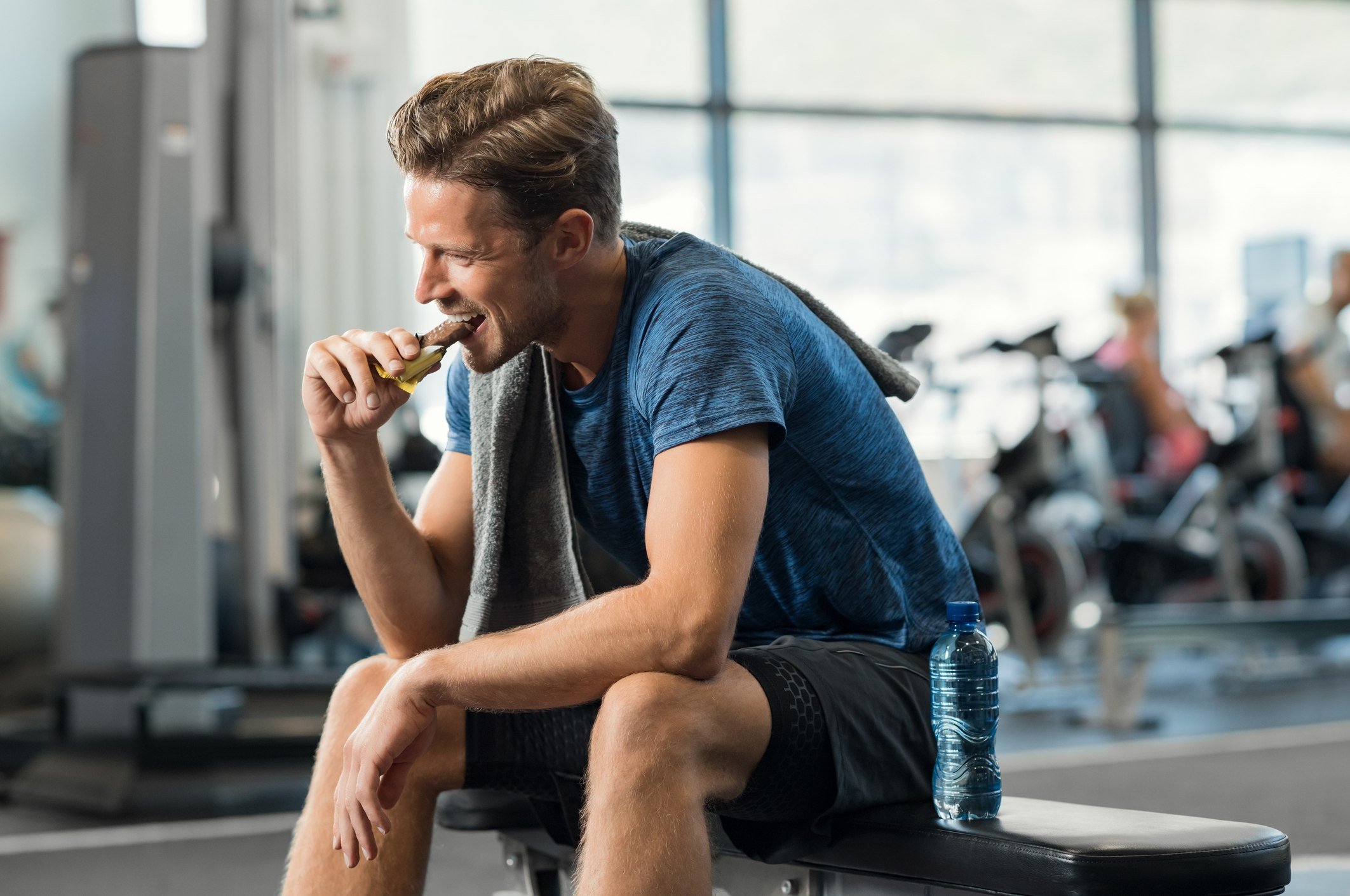 Sweaty young man eating energy bar at gym