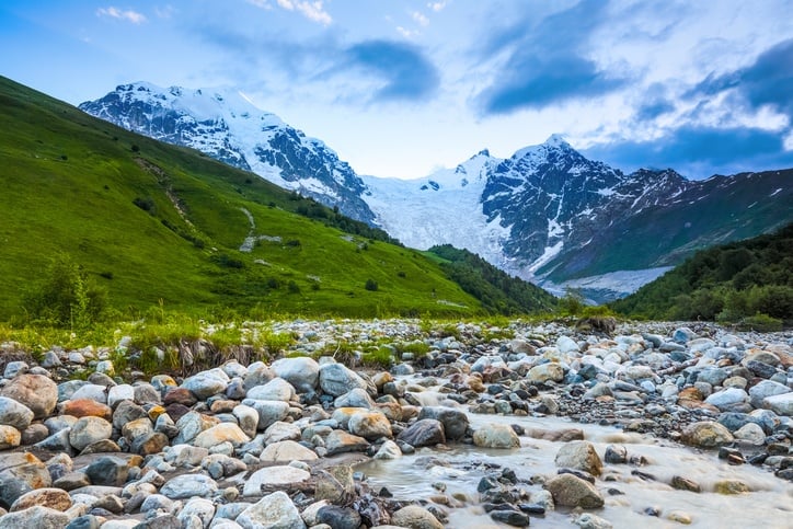 From the river shore, covered with stones, opens view on fantastic glacier and steep rocky mountains with green meadows, which are covered with snow.Happy lifestyle. Beautiful universe.