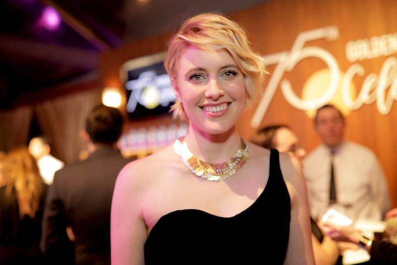 Greta Gerwig smiles while posing in a black dress and gold necklace. Greta Gerwig smiles while posing in a black dress and gold necklace.