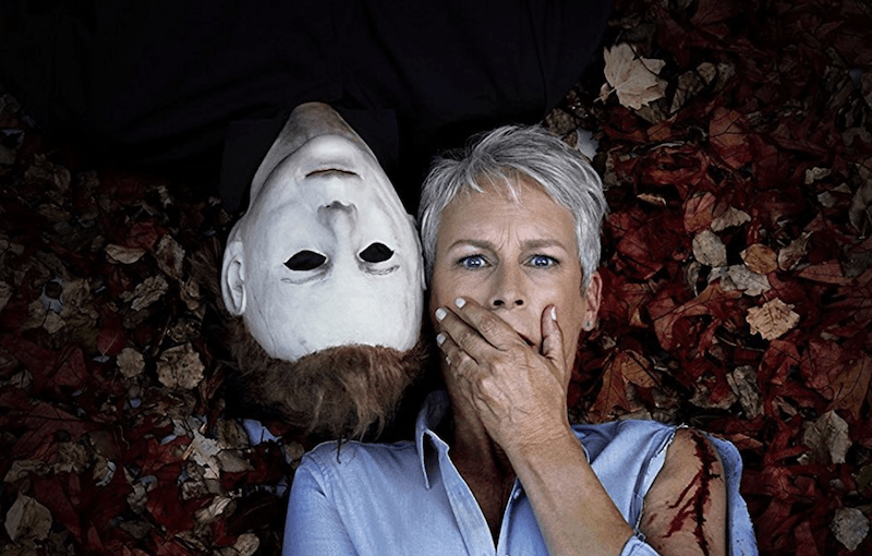 Jaime Lee Curtis laying on a ground of leaves next to a strange figure in 'Halloween'.