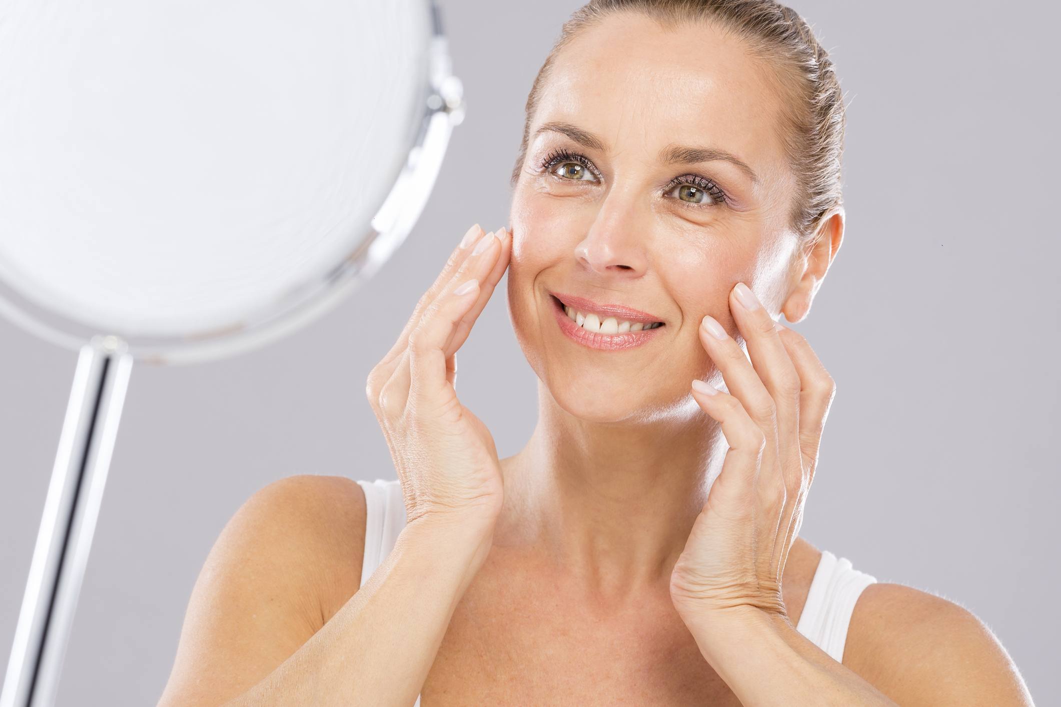 Mature woman applying moisturizer to her skin in a mirror