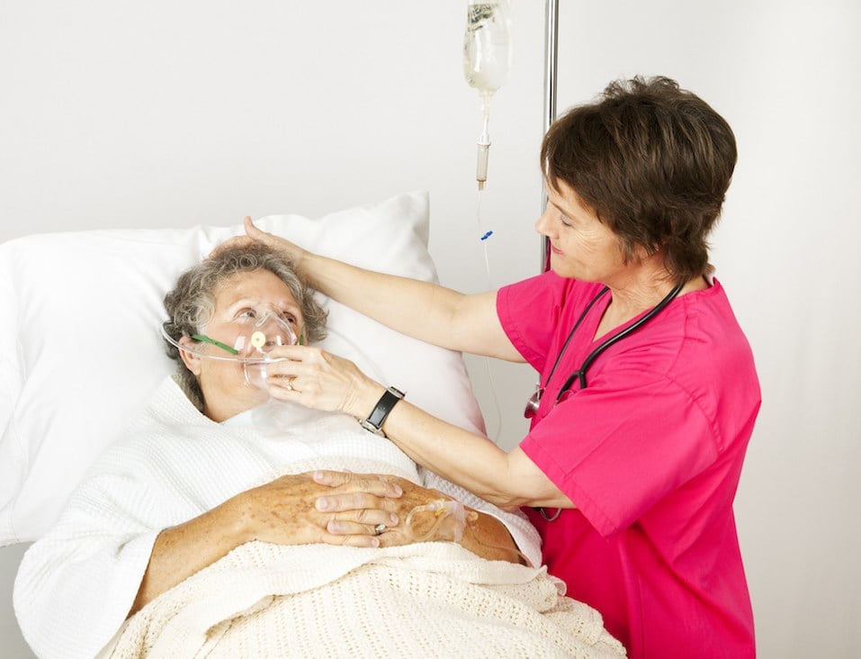 Hospital nurse helps a senior woman breath through an oxygen mask