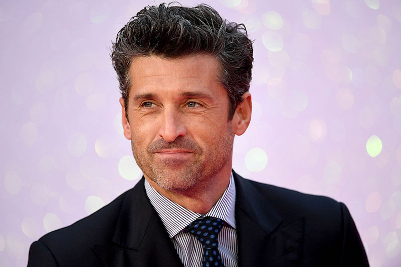 Patrick Dempsey in a suit and tie behind a purple background.