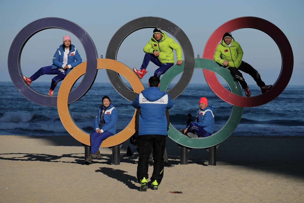 Members of the Mongolian ski team take selfies with the Olympic Rings on the beach at Gangneung