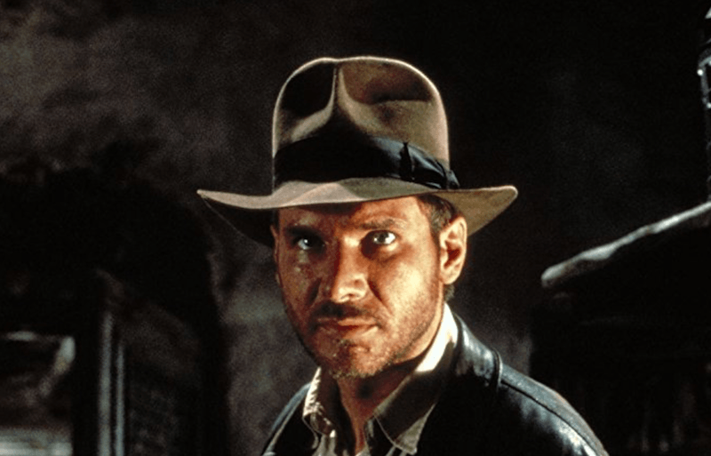 Indiana Jones looking straight ahead while wearing a hat and jacket. Indiana Jones looking straight ahead while wearing a hat and jacket.