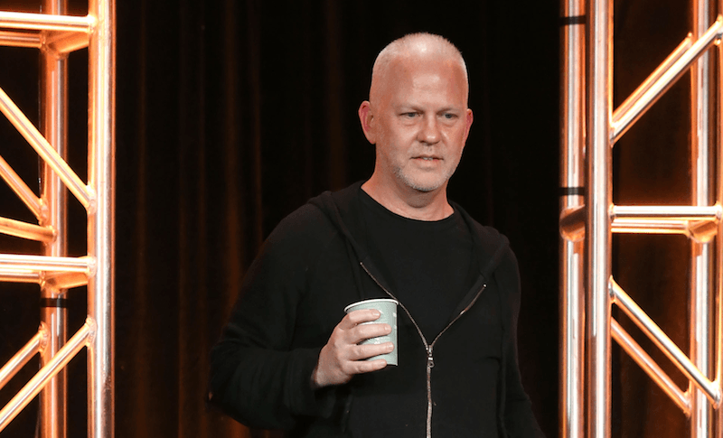 Ryan Murphy walking on stage holding a plastic cup.