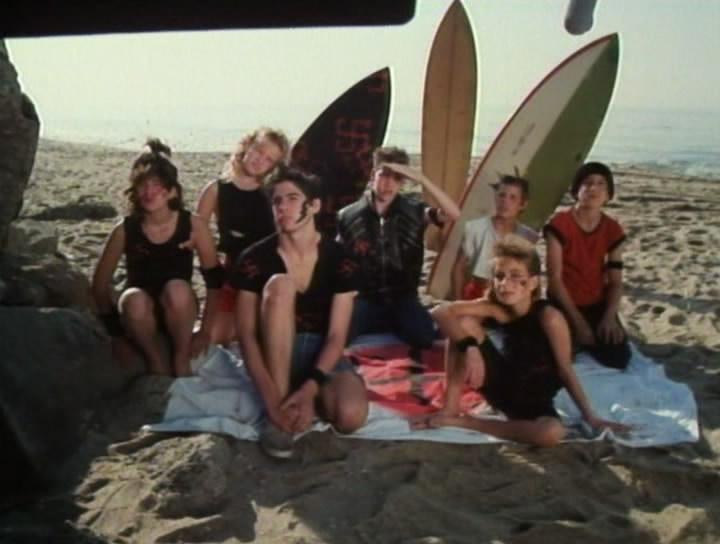 a group of people sits on a towel in the sand with surfboards a group of people sits on a towel in the sand with surfboards