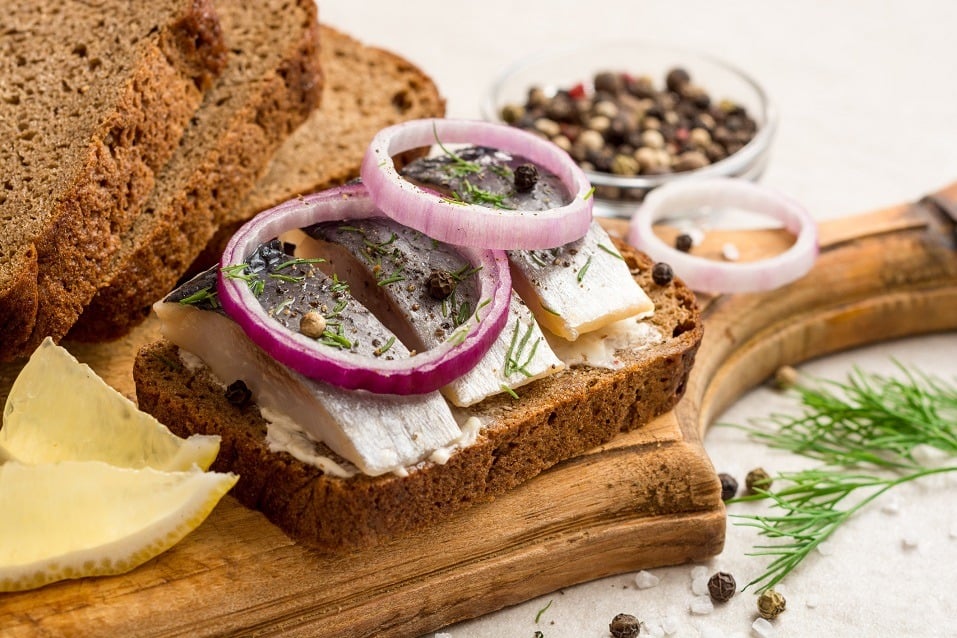 Sandwich with salted herring, butter and red onion on old rustic cutting board