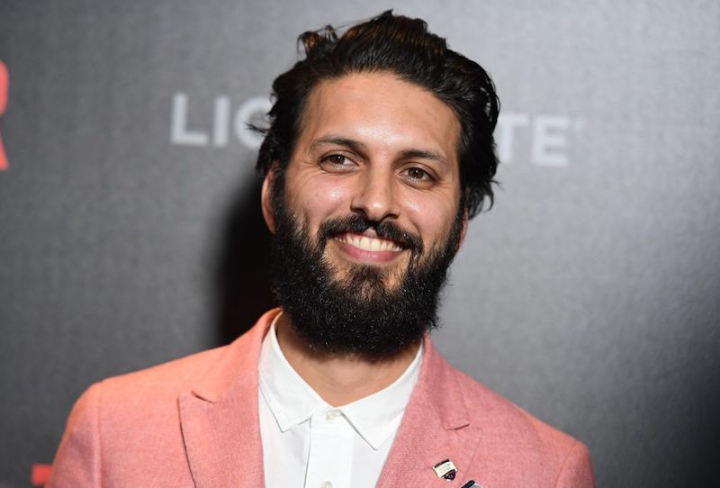 Latif smiles while wearing a salmon colored blazer and white shirt on a red carpet. Latif smiles while wearing a salmon colored blazer and white shirt on a red carpet.