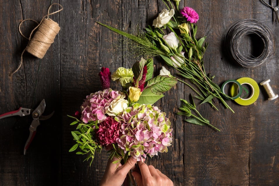 The hands of florist against desktop with working tools and ribbons