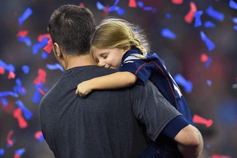 Tom Brady holding his daughter at a game. 