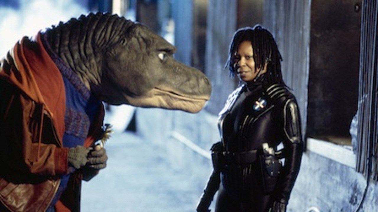 Whoopi Goldberg stands in front of a dinosaur