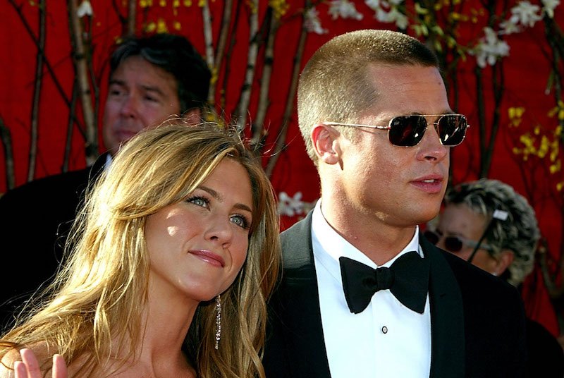 Jennifer Aniston smiling and waving as she poses with Brad Pitt. 