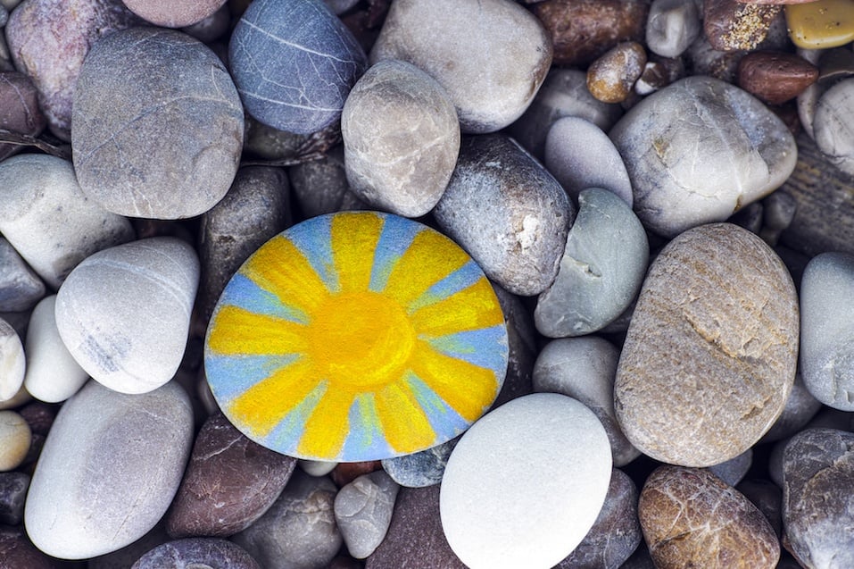 Bright sun painted on pebble with stones background