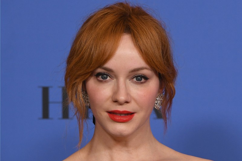 Christina Hendricks wearing red lipstick and jeweled earrings on a red carpet.