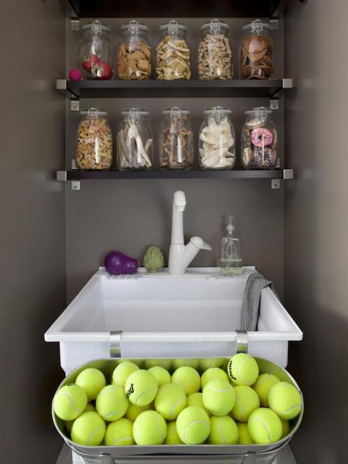 A silver container of golf balls, a white sink and a cabinet of dog treats on a wall. A silver container of golf balls, a white sink and a cabinet of dog treats on a wall.