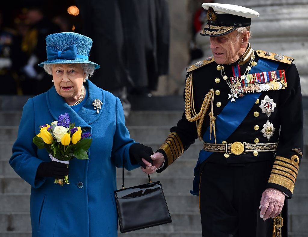 Queen Elizabeth and Prince Philip hold hands as they walk down steps. 