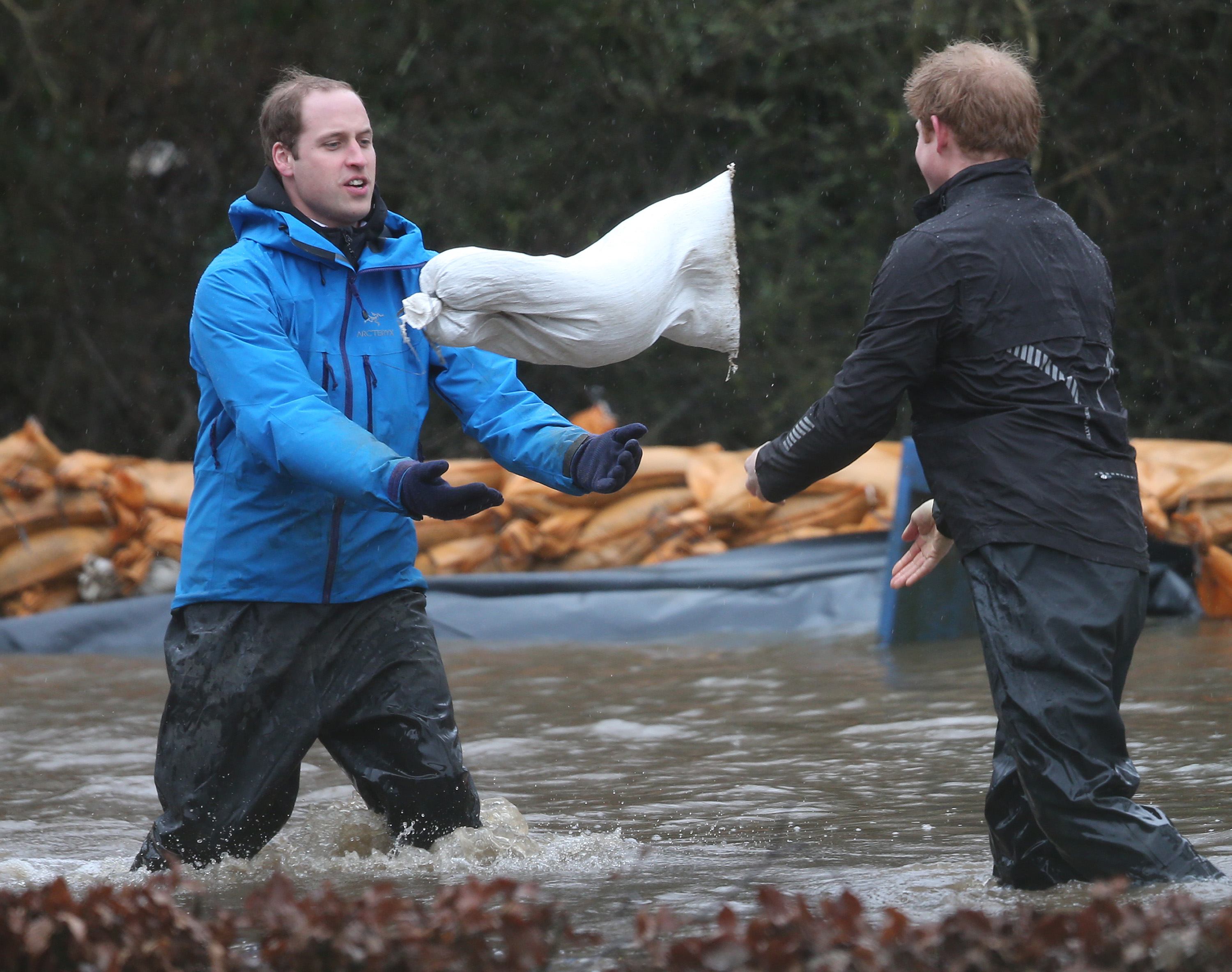 Prince William, Duke of Cambridge (L) catches a sandbag thrown by his brother Prince Harry as they build a flood wall