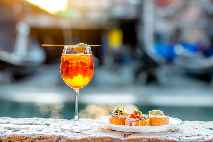 Spritz Aperol drink with venetian traditional snacks cicchetti on the water chanal background in Venice. Traditional italian aperitif. 