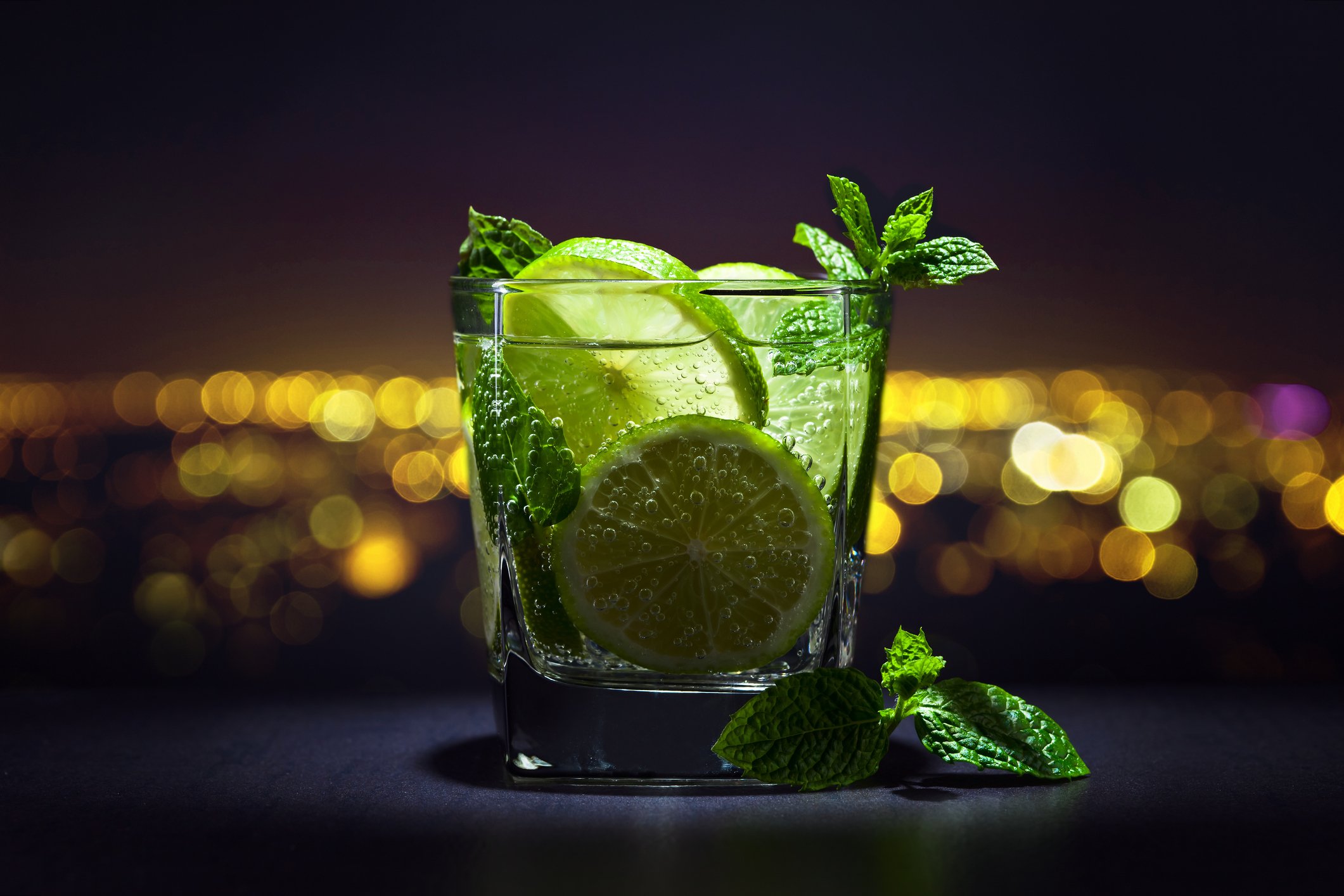 Drink with lime , ice and peppermint leaves on a background of night city