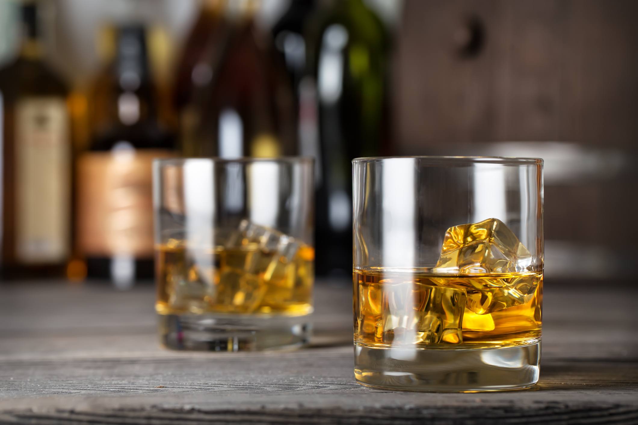Two glasses of whiskey with ice on the bar counter against the bottles