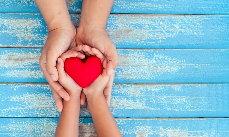 Red heart in child kid and mother hands on old blue wooden table in vintage retro style Red heart in child kid and mother hands on old blue wooden table in vintage retro style