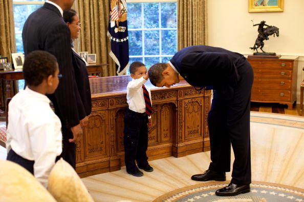 Obama bends over so the son of a White House staff member can pat his head during a visit to the Oval Office Obama bends over so the son of a White House staff member can pat his head during a visit to the Oval Office