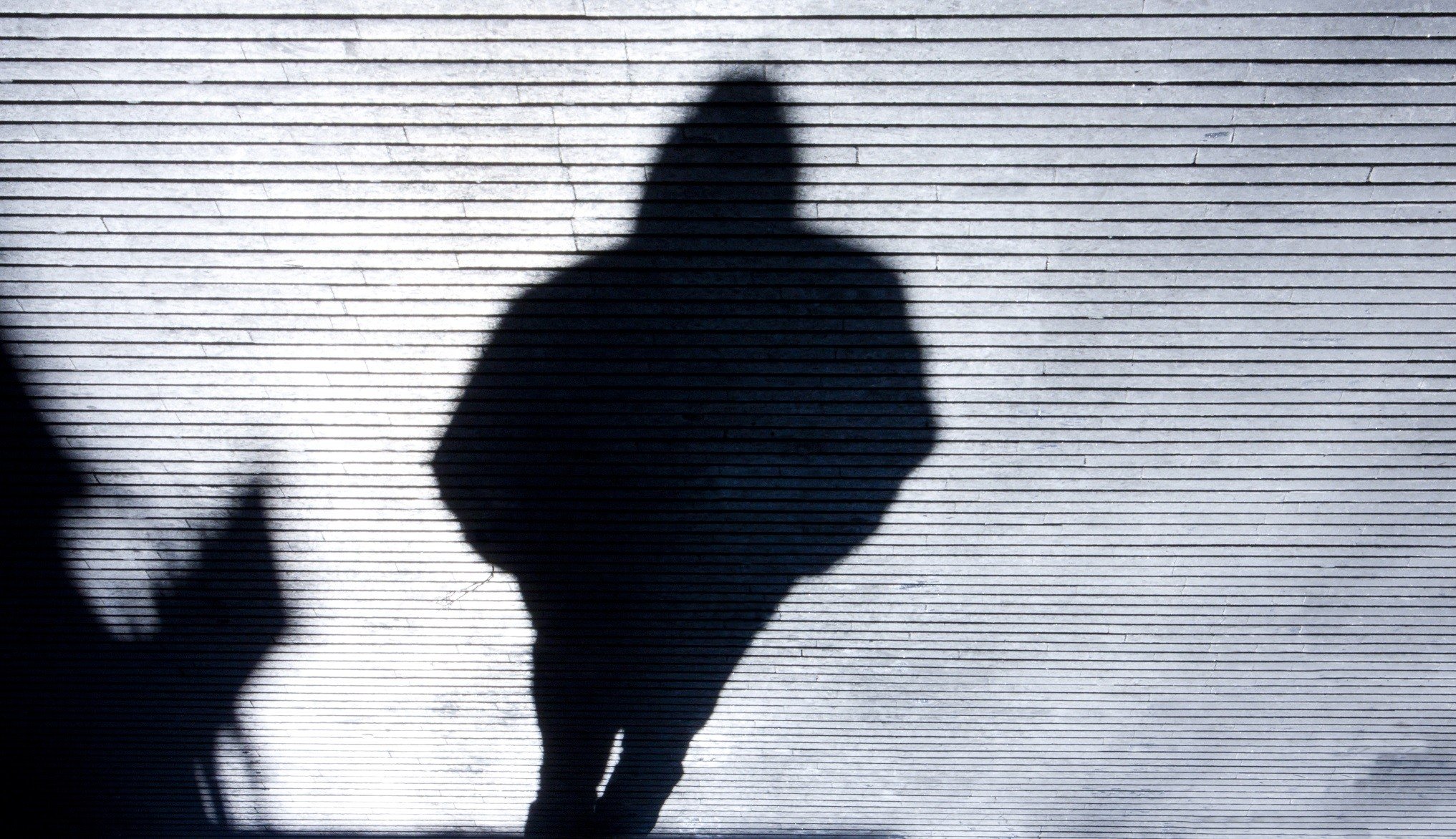Shadow of person walking with hands in pockets and hood up