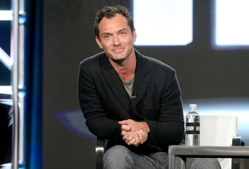Jude law sits and smiles while on an on-stage panel. 