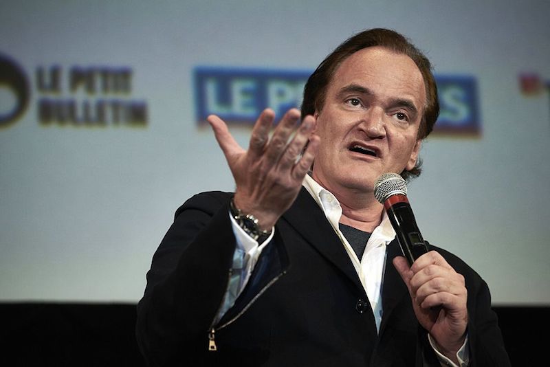 Quentin Tarantino holding a microphone and speaking on stage.