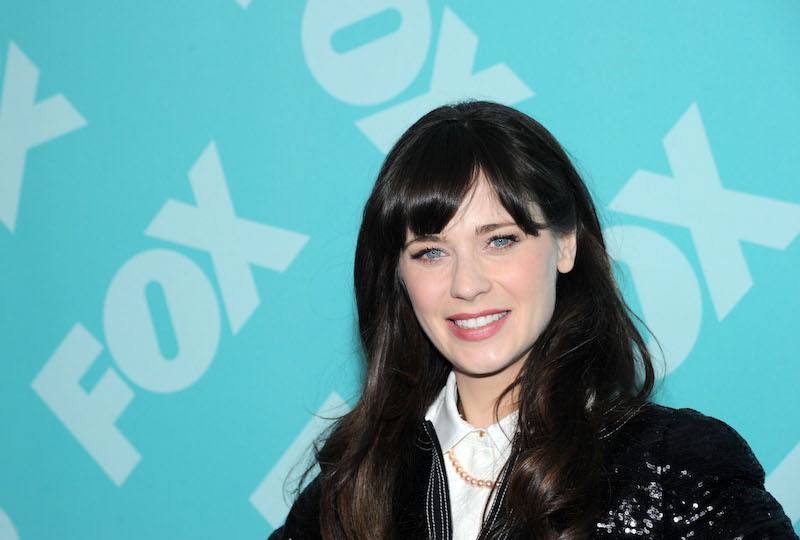 Zooey Deschanel smiling in front of a blue background. 