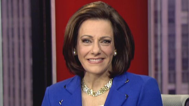 K.T. McFarland smiles while wearing a blue jacket and gold jewelry