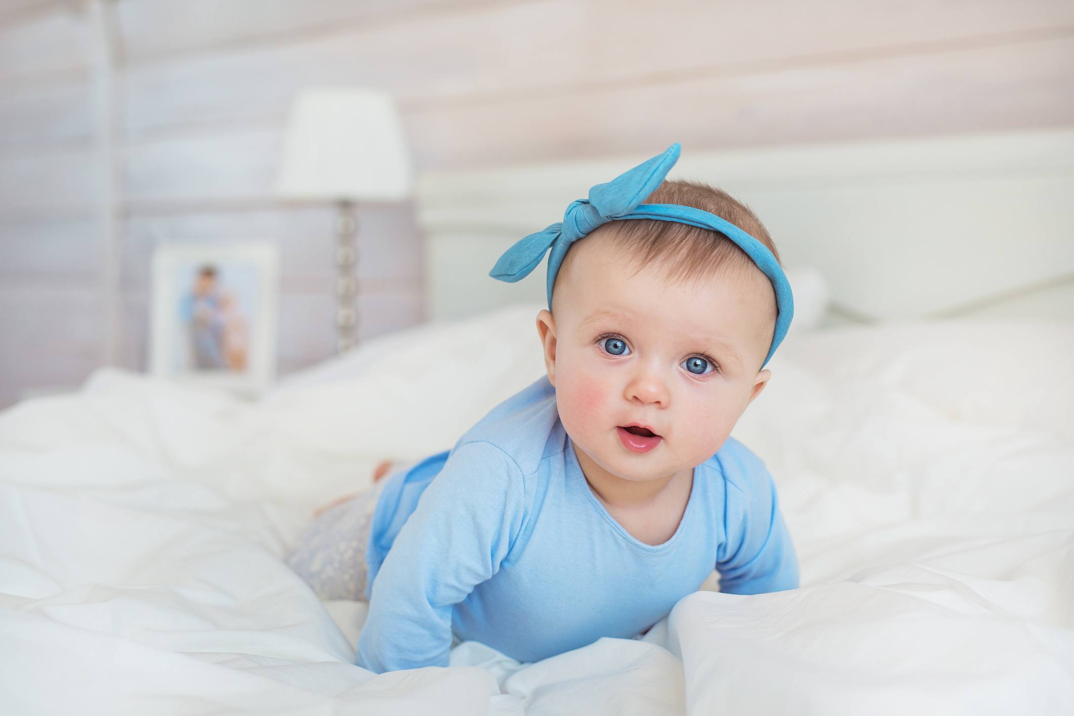 Baby crawling in light blue outfit on a bed
