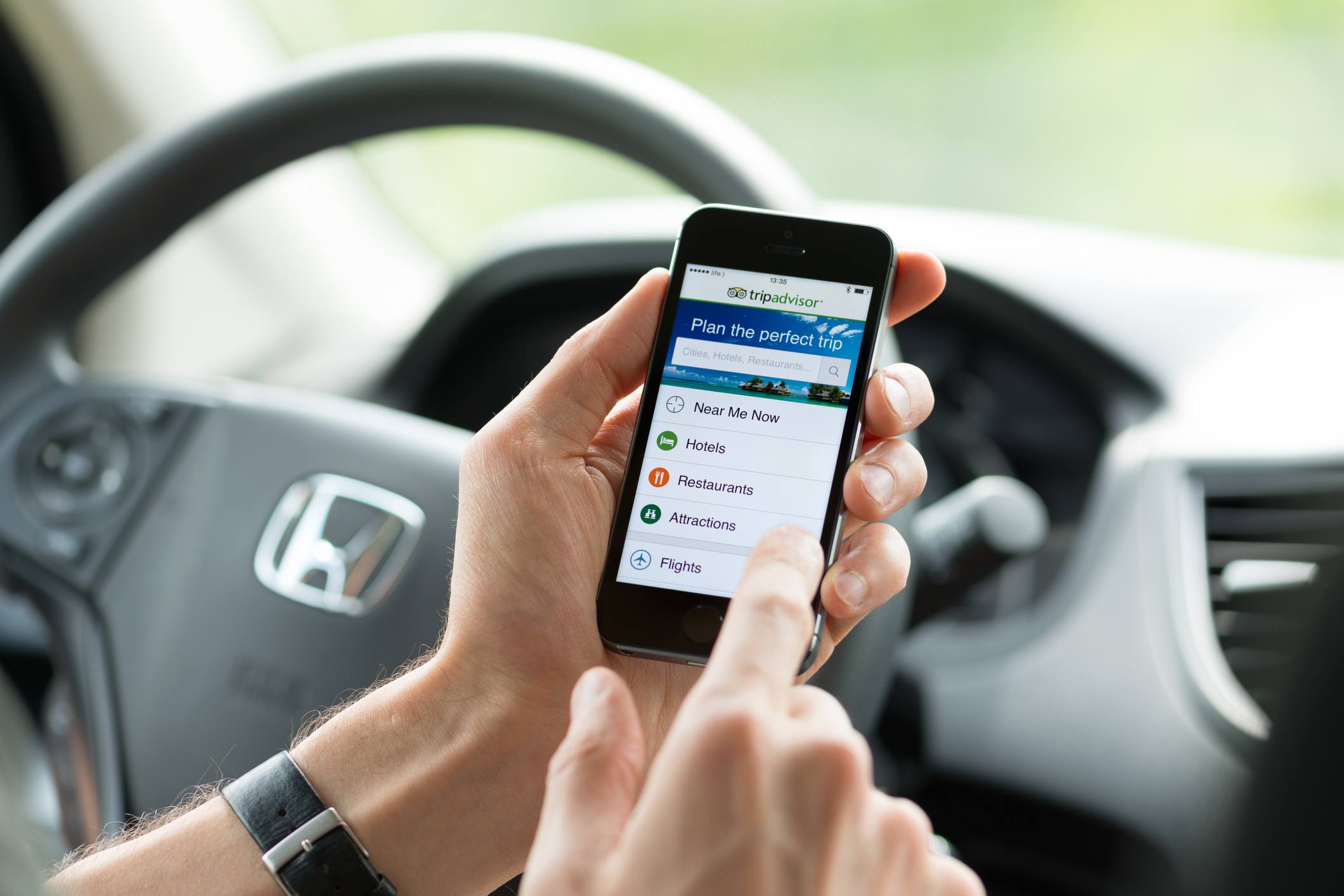 Man in car with TripAdvisor app open.